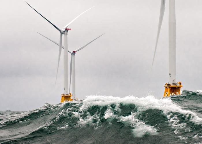 View of two wind turbines in turbulent grey sea with waves