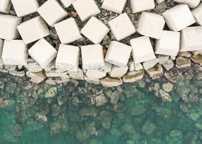 Aerial view of white armoured breakwater in green sea waves